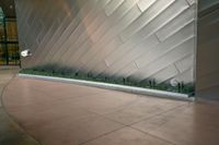 the entrance is tiled with silver and concrete patterns in the building's walls as well as some green grass