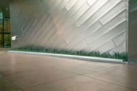 the entrance is tiled with silver and concrete patterns in the building's walls as well as some green grass