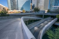 a curved walkway in front of a river in a city with tall buildings and tall trees