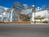 silver building with a curved design near an intersection and a city street scene behind it