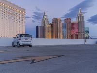 a white minivan parked in a parking lot outside a city building with an roller coaster