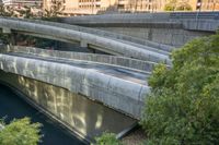 a large concrete bridge over a river next to buildings in a city environment where people are traveling down the bridge