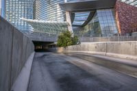 some glass and metal building a long highway and buildings a bench and a road with trees on it