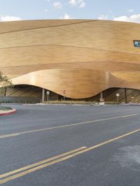 the modern looking building with golden roof is on the corner of the street with cars passing by