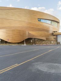 the modern looking building with golden roof is on the corner of the street with cars passing by