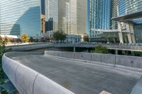 concrete walkway alongside road near skyscraper buildings in city setting and reflection on glass windowed wall