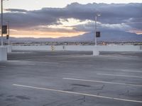 a parking lot with the sun shining on the horizon and mountains in the distance as clouds gather in the background