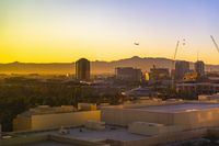 a photo of some buildings and trees and mountains in the distance as the sun sets