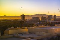 a photo of some buildings and trees and mountains in the distance as the sun sets