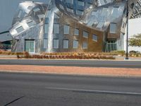 an abstract building with large silver sculptures and trees along the side of the street in front of it