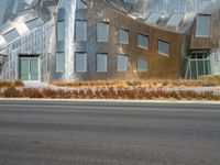 a view from the side of a road of a building with a silver facade, some grass, and trees