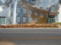 a view from the side of a road of a building with a silver facade, some grass, and trees