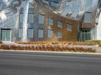 a view from the side of a road of a building with a silver facade, some grass, and trees