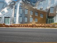 a view from the side of a road of a building with a silver facade, some grass, and trees