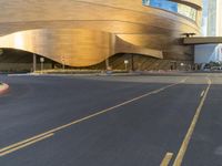 a street view of a curved metallic building in a city with traffic passing by it