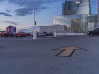 the parking lot has an arrow sign on it, near two buildings and a park