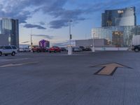 the parking lot has an arrow sign on it, near two buildings and a park