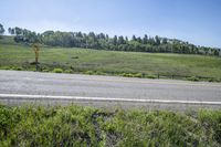 a empty highway with an open field and woods in the distance on a sunny day