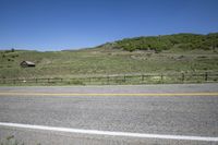 a black van is driving down a road that passes between mountains with bushes, fences and a wooden fence