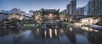 an asian garden is surrounded by buildings at night time at dusk in the evening, with water running over the patio area