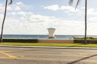 a lifeguard chair that is on the grass and beside the ocean with some palm trees