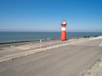 a lighthouse standing on the beach at the edge of a road that leads to water