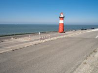 a lighthouse standing on the beach at the edge of a road that leads to water