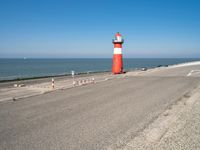 a lighthouse standing on the beach at the edge of a road that leads to water