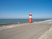 a lighthouse standing on the beach at the edge of a road that leads to water