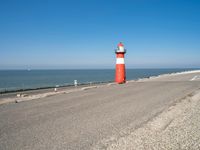 a lighthouse standing on the beach at the edge of a road that leads to water