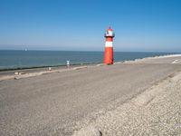 a lighthouse standing on the beach at the edge of a road that leads to water