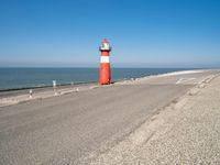 a lighthouse standing on the beach at the edge of a road that leads to water