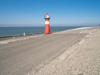 a lighthouse standing on the beach at the edge of a road that leads to water