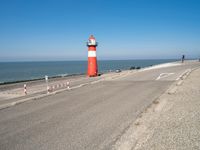 a lighthouse standing on the beach at the edge of a road that leads to water