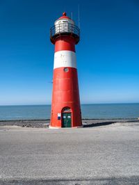 a tall red and white lighthouse on a beach next to the ocean with a blue sky