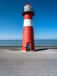 a tall red and white lighthouse on a beach next to the ocean with a blue sky