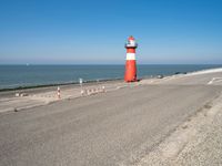 a large lighthouse is standing on the edge of the road by the ocean in the distance