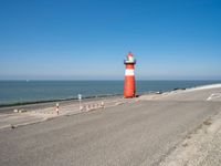 a large lighthouse is standing on the edge of the road by the ocean in the distance