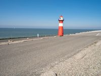 a large lighthouse is standing on the edge of the road by the ocean in the distance