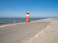 a large lighthouse is standing on the edge of the road by the ocean in the distance