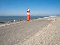 a large lighthouse is standing on the edge of the road by the ocean in the distance