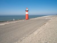 a large lighthouse is standing on the edge of the road by the ocean in the distance