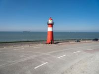 an orange and white lighthouse is next to the ocean near some cars and people on the road