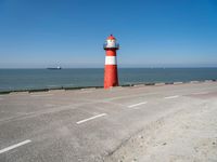 an orange and white lighthouse is next to the ocean near some cars and people on the road