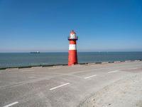 an orange and white lighthouse is next to the ocean near some cars and people on the road