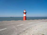 an orange and white lighthouse is next to the ocean near some cars and people on the road