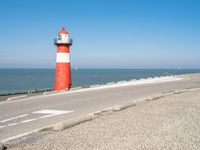 a lighthouse sits on a road next to the ocean and a beach with cars and bikes