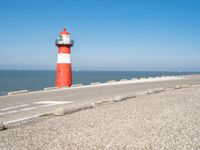 a lighthouse sits on a road next to the ocean and a beach with cars and bikes