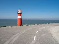 the road has a light house with a red top on the top of it next to the ocean