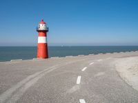 the road has a light house with a red top on the top of it next to the ocean